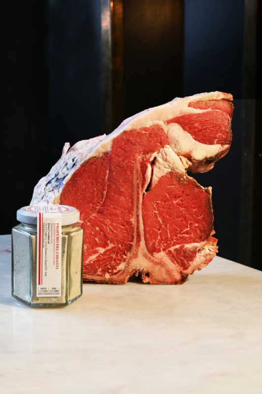 Bistecca Fiorentina cut of meat next to a jar of Chianti seasoning on a marble surface.