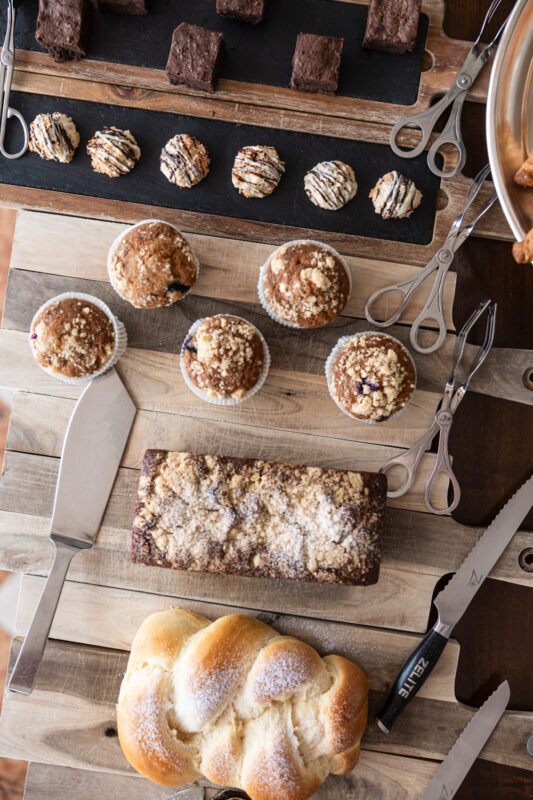 Assorted baked goods including brownies, muffins, and a loaf of challah on a wooden table.