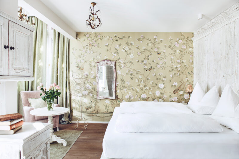 Elegant junior suite at Castel Fragsburg featuring floral wallpaper, a mirror, and a cozy seating area with a bouquet of r...