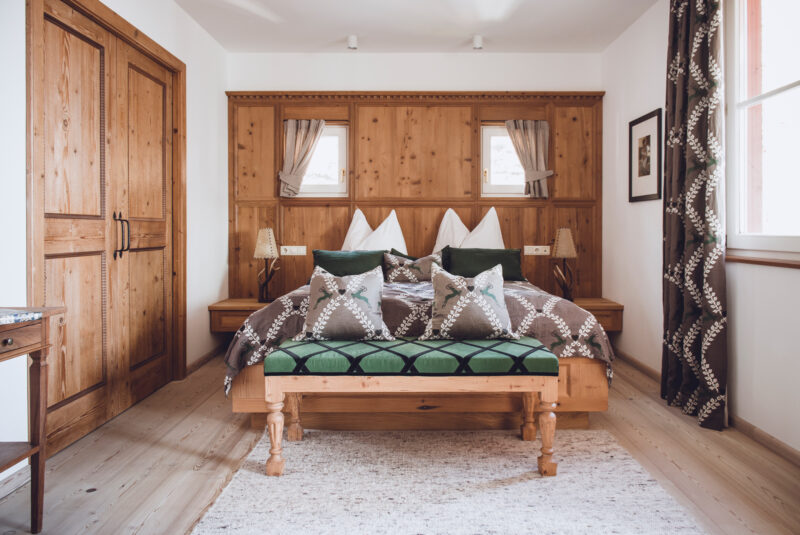 Deluxe suite at Castel Fragsburg featuring a wooden bed, decorative pillows, and natural light from large windows.