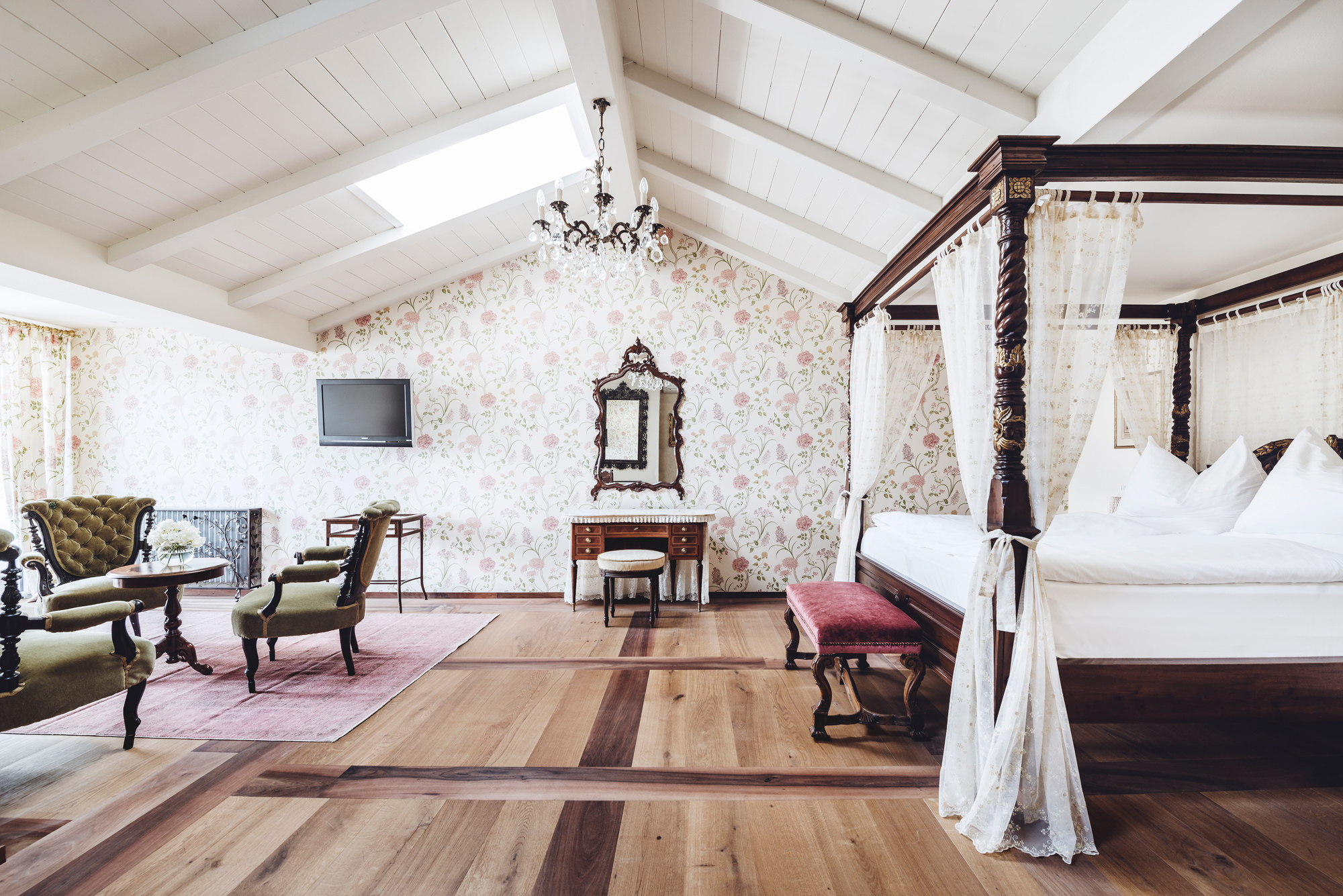 Luxurious suite at Castel Fragsburg featuring a four-poster bed, vintage furniture, floral wallpaper, and wooden flooring.