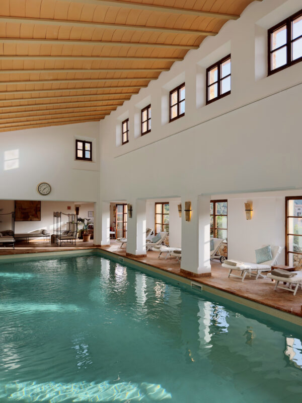 Indoor swimming pool with lounge chairs, large windows, and wooden ceiling at La Residencia.