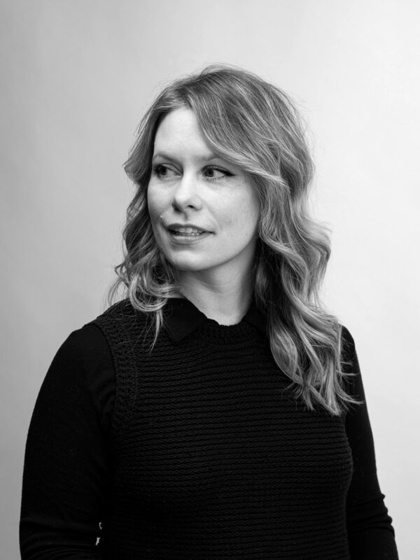 Black and white portrait of a woman with wavy hair, wearing a black top, looking to the side against a light background.