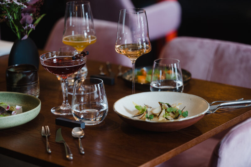 Elegant table setting at Restaurant Brikz featuring cocktails, wine, and a gourmet dish with fresh herbs.
