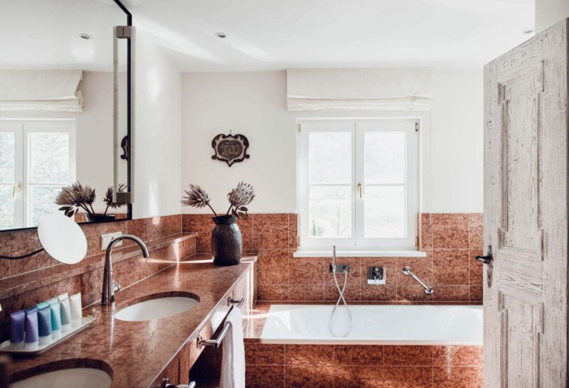 Luxurious bathroom featuring a marble countertop, double sinks, a freestanding bathtub, and natural light from a window.
