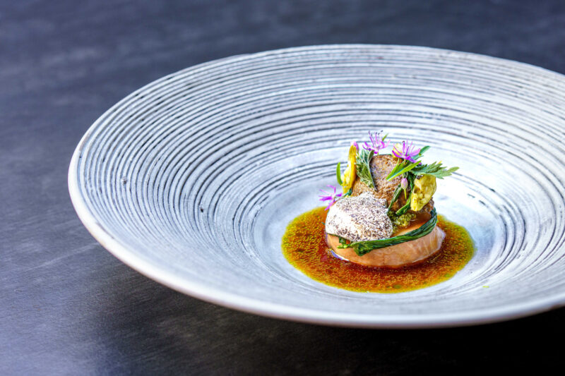 Plated dish featuring Husumer lamb, morel mushrooms, and wild garlic, garnished with herbs and edible flowers.