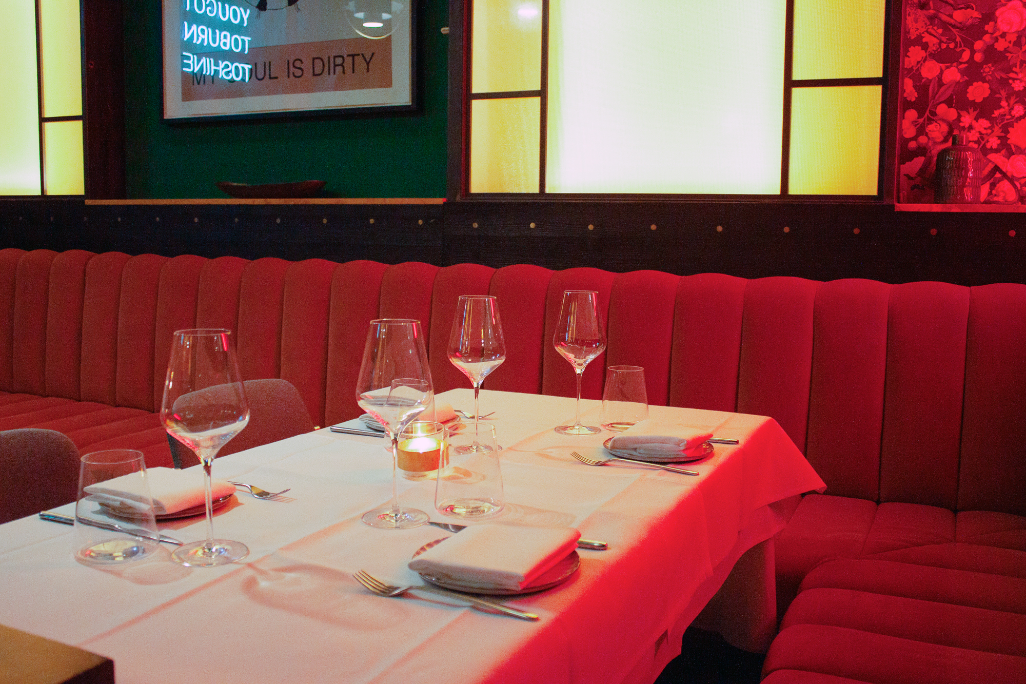 Elegant restaurant table set with wine glasses and candles, surrounded by red upholstered seating.