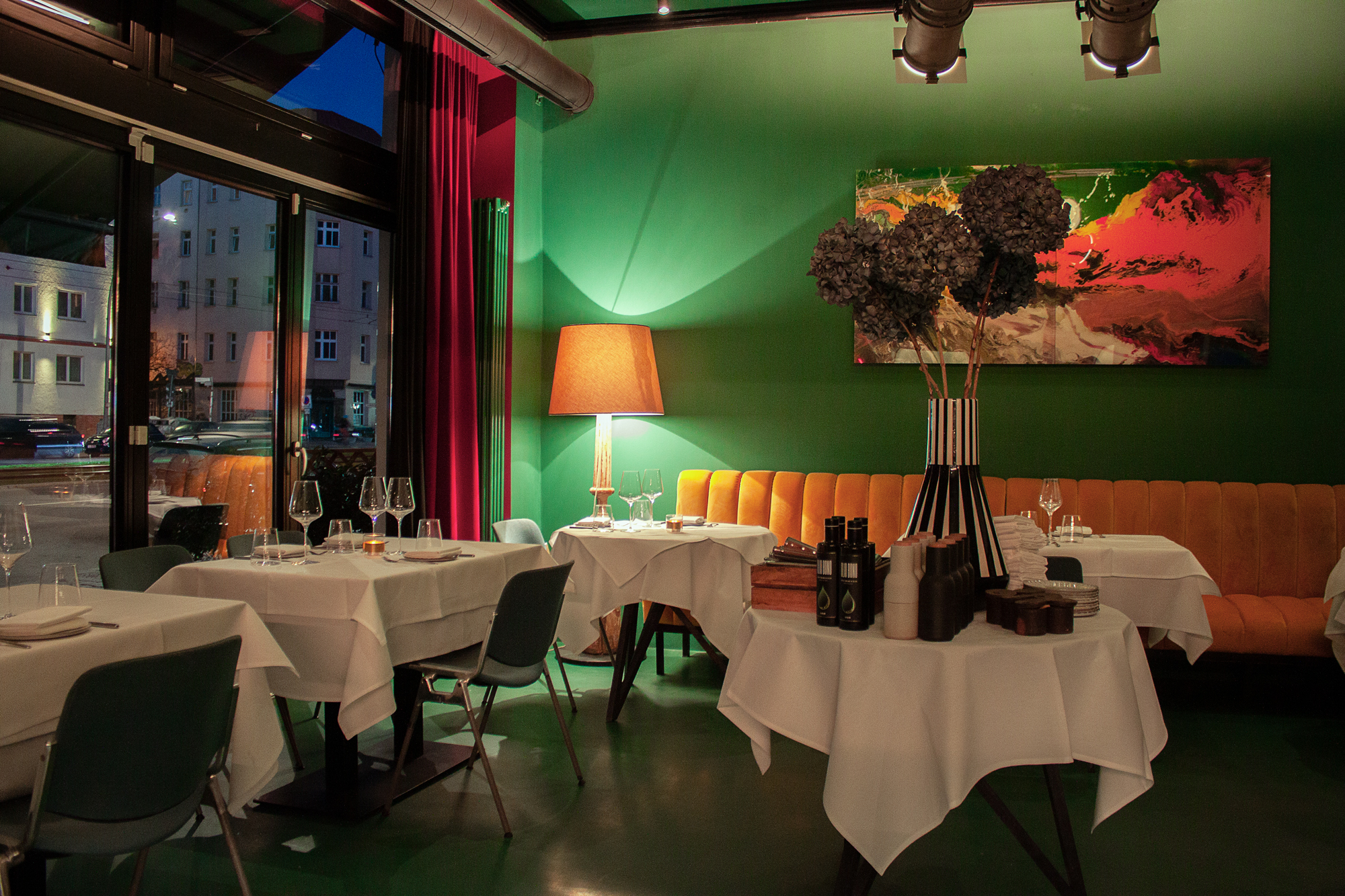 Elegant restaurant interior with green walls, orange seating, and artistic decor, featuring tables set for dining.