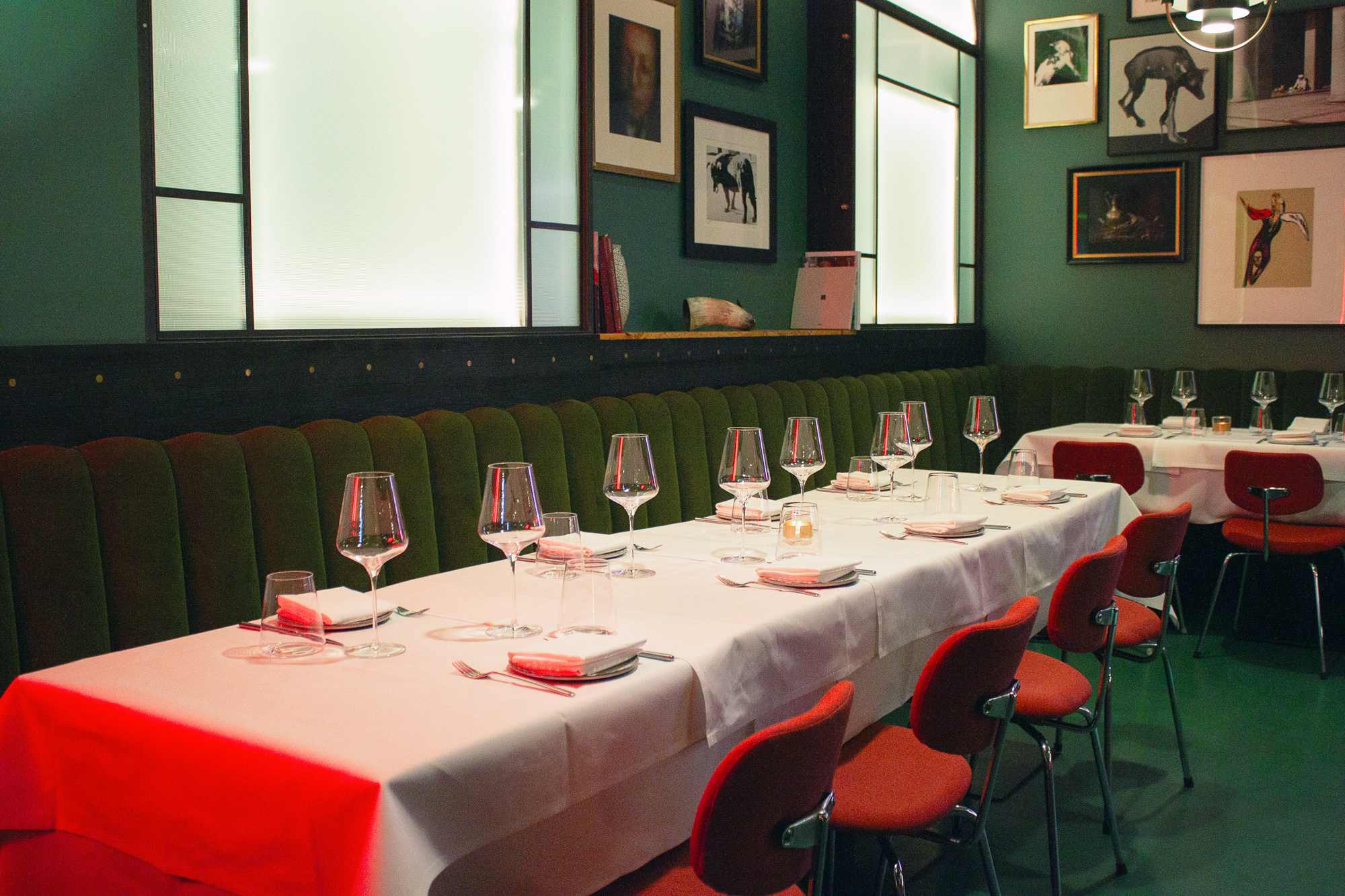 Elegant dining setup with a long table, green velvet seating, and wine glasses, in a stylish restaurant interior.