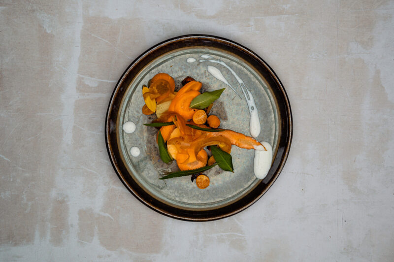 Colorful dish featuring sliced carrots, green leaves, and dollops of kefir sauce on a textured plate.