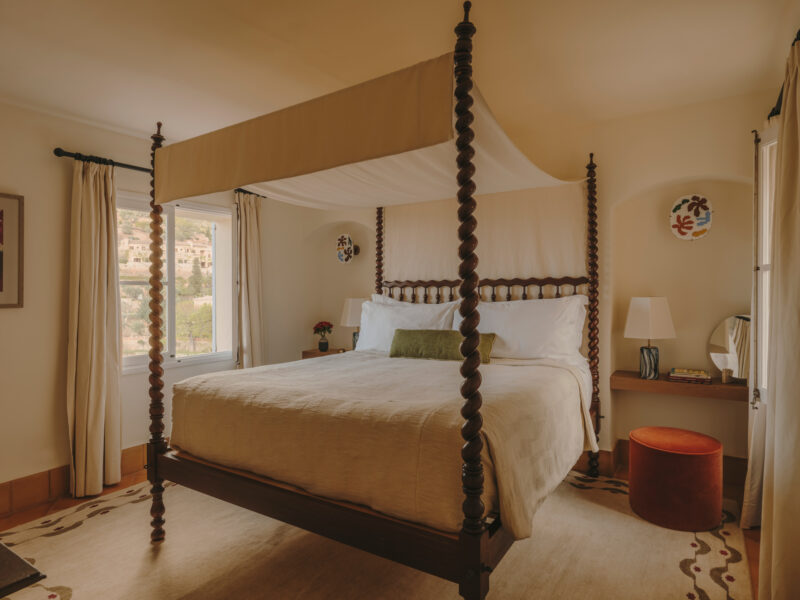 Cozy bedroom featuring a four-poster bed, soft linens, and a view through a window, with decorative elements on the walls.