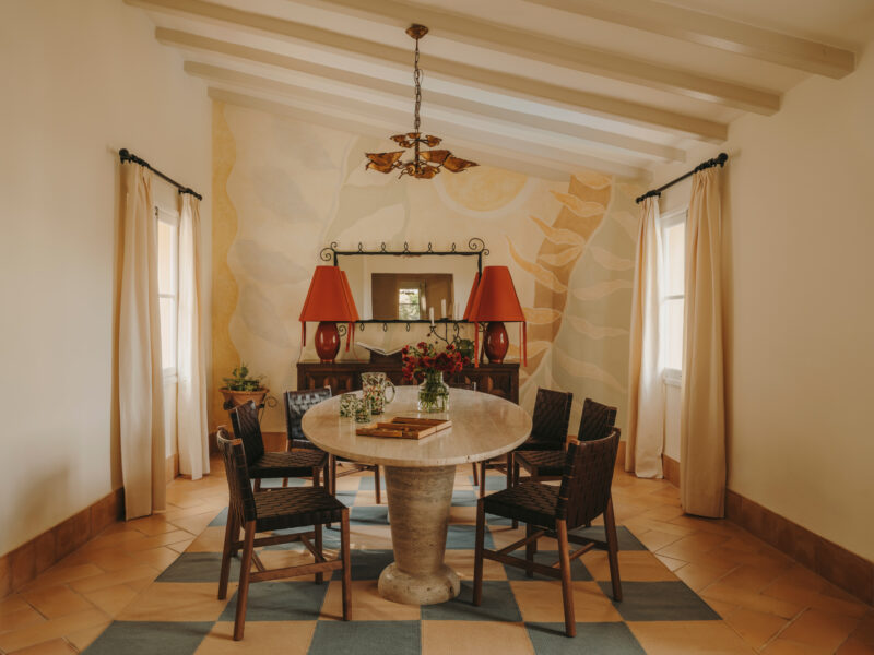 Dining area featuring a round table, four chairs, two red lamps, and a decorative wall mural in soft colors.