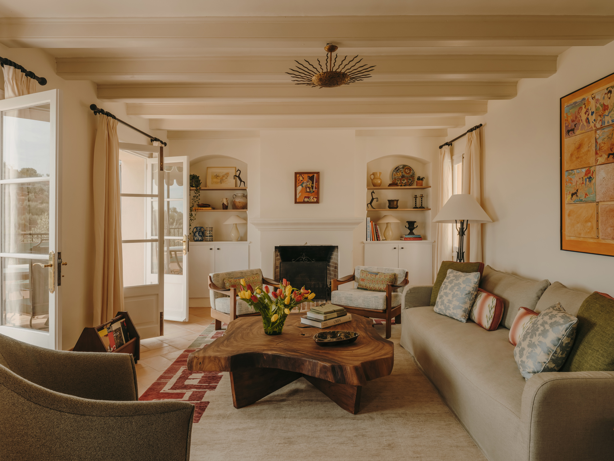Cozy living room with a wooden coffee table, floral arrangement, and light-colored furniture, featuring large windows and ...