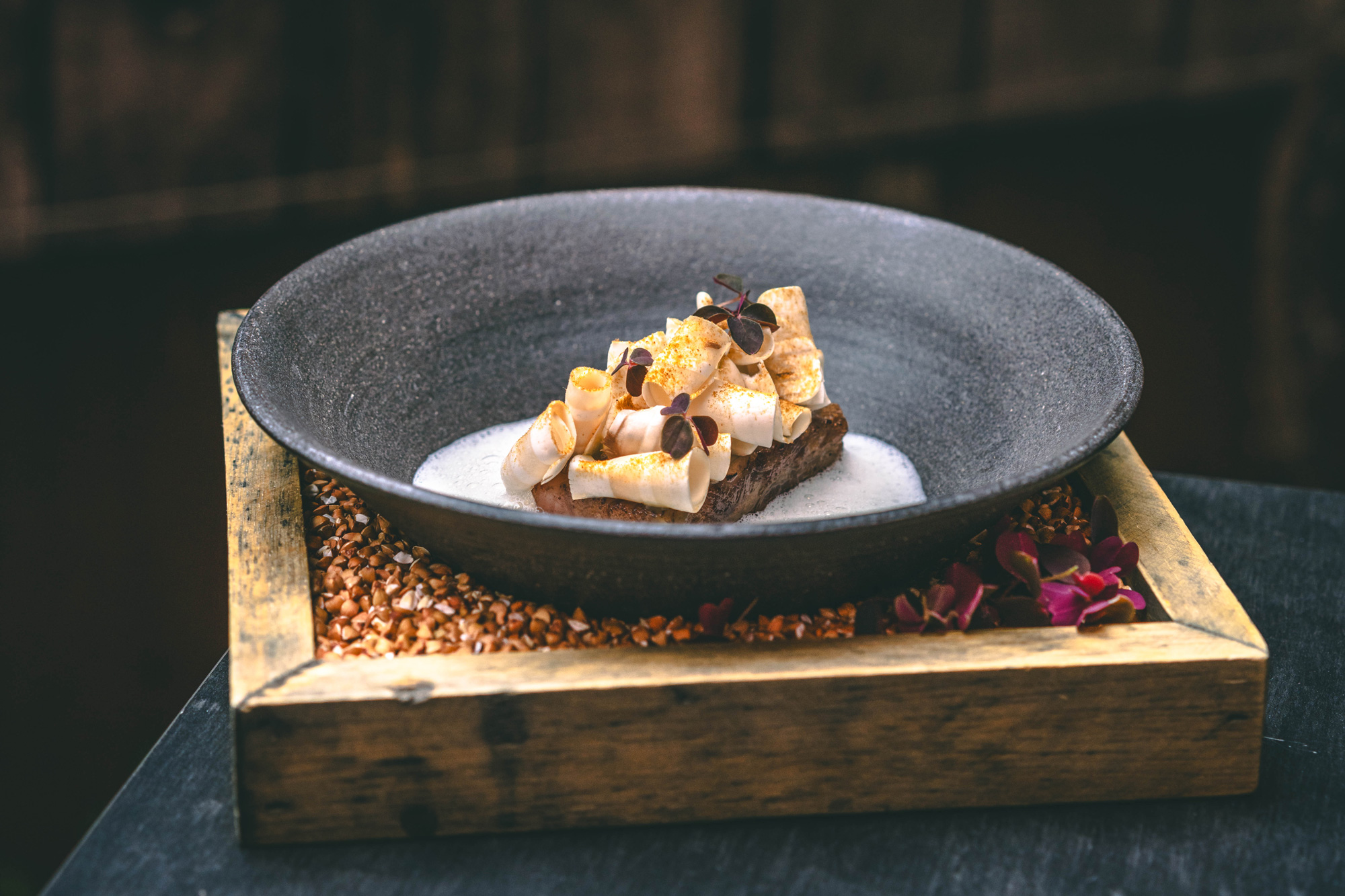 Oldenburger Wagyu beef served with sour cherries and shallots, garnished with microgreens in a dark bowl.