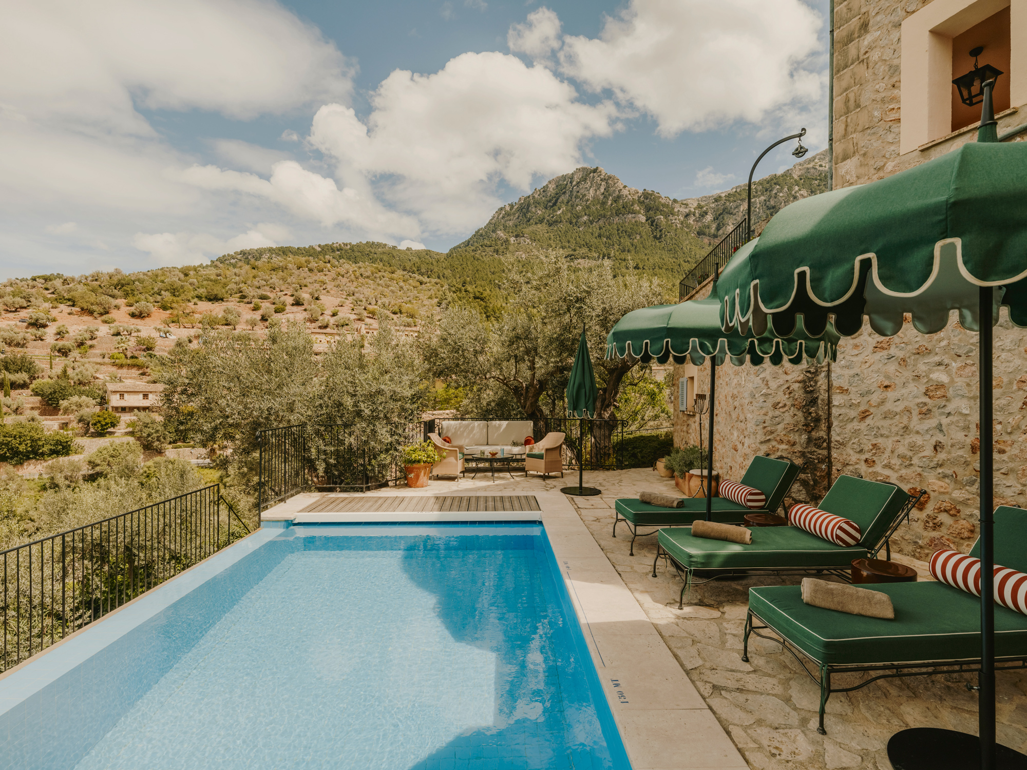 Mountain view from a terrace featuring a swimming pool, lounge chairs, and green umbrellas at La Residencia.