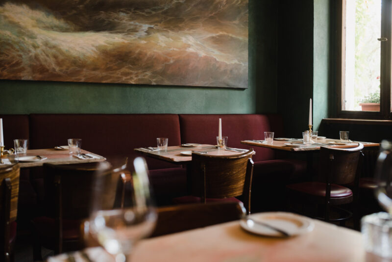 Elegant restaurant interior with wooden tables, burgundy seating, and a large abstract painting on the wall.