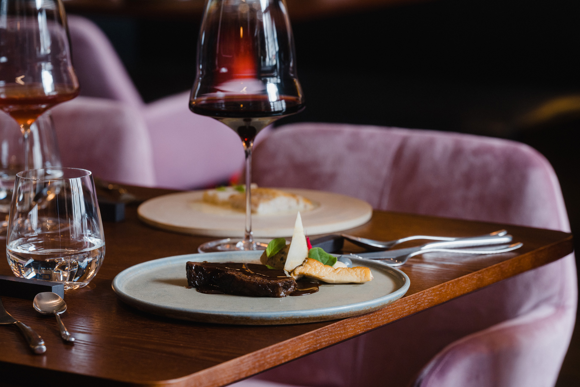 Plate featuring braised beef cheek with celery and mushroom, garnished with green herbs, set on a wooden table in a restau...