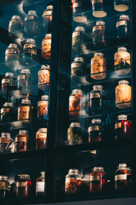 Glass display filled with jars containing various preserved foods, illuminated in a modern restaurant interior.