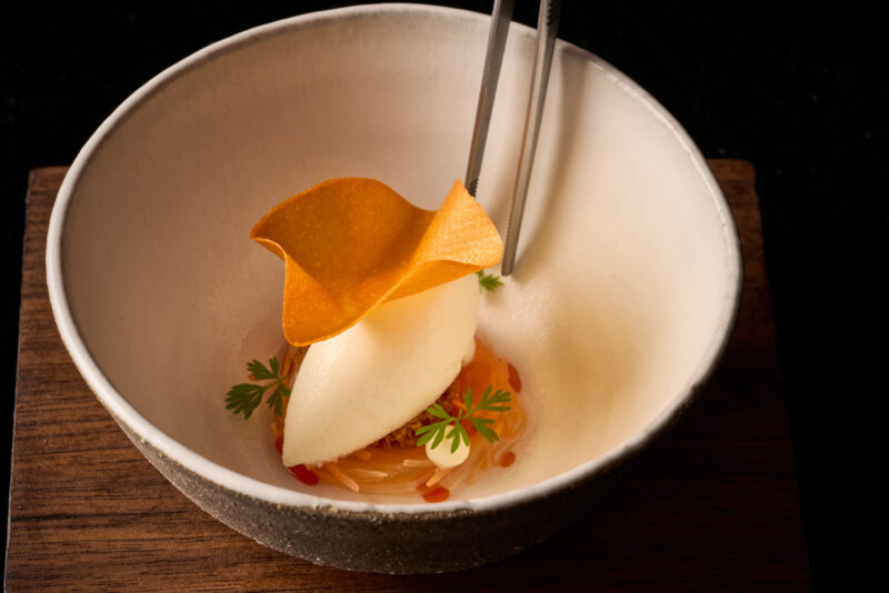 Delicate dessert featuring a scoop of white ice cream, orange crisp, and garnished with herbs in a bowl.