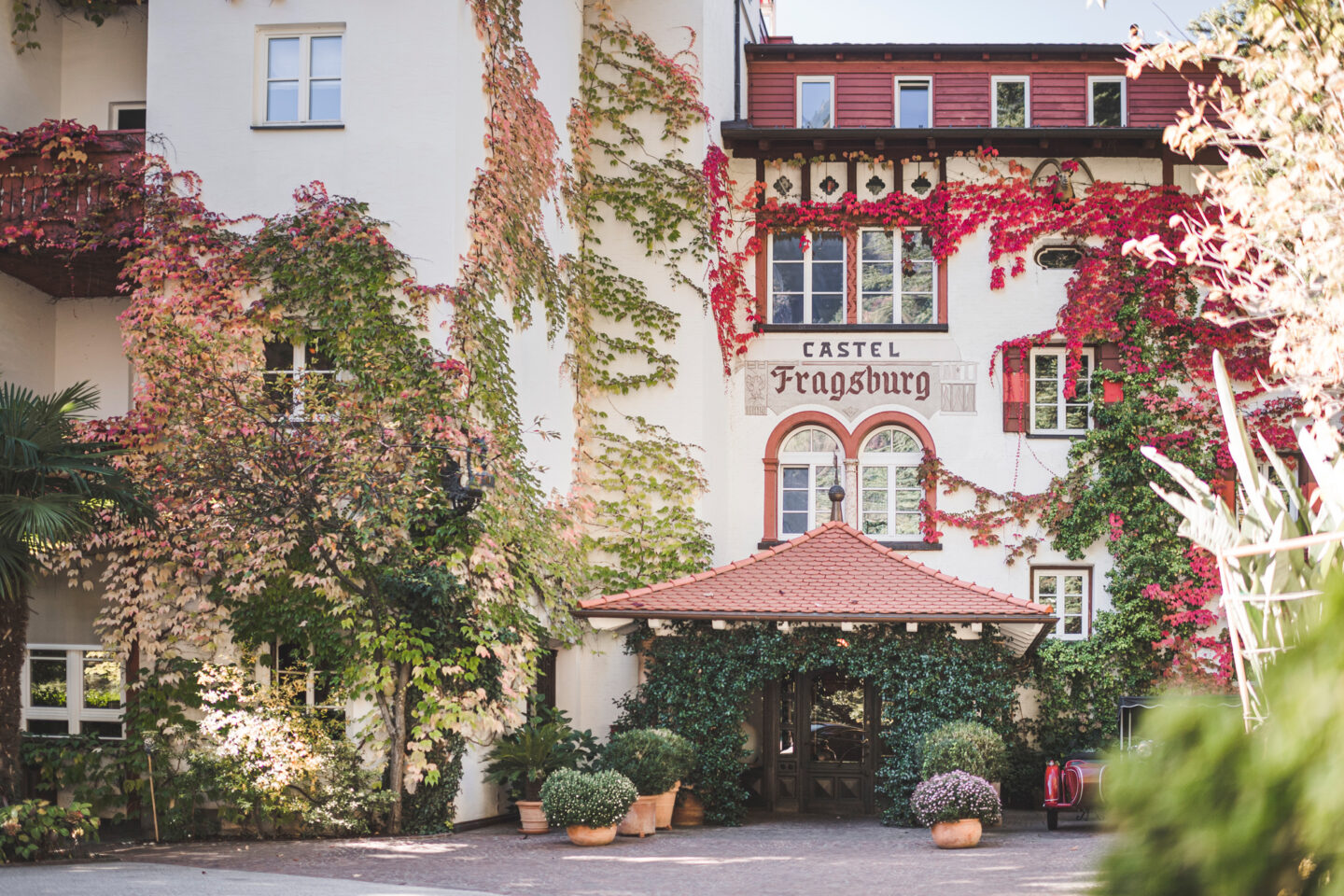 Castel Fragsburg entrance adorned with colorful ivy and greenery, featuring a red-tiled roof and welcoming atmosphere.