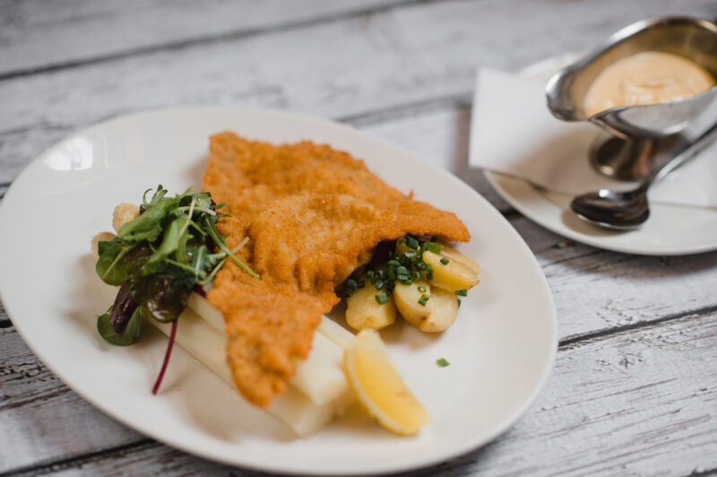 Crispy schnitzel served with lemon, potatoes, and a side of salad, accompanied by a small bowl of sauce.