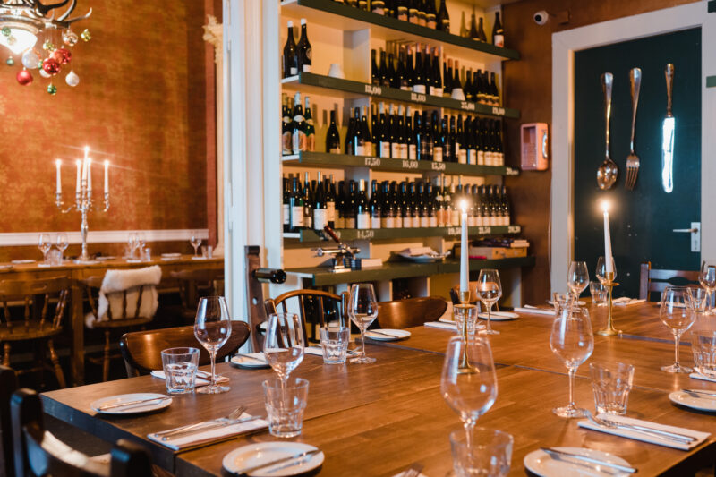 Elegant dining setup with a wooden table, wine bottles on shelves, and candlelight in a cozy restaurant setting.