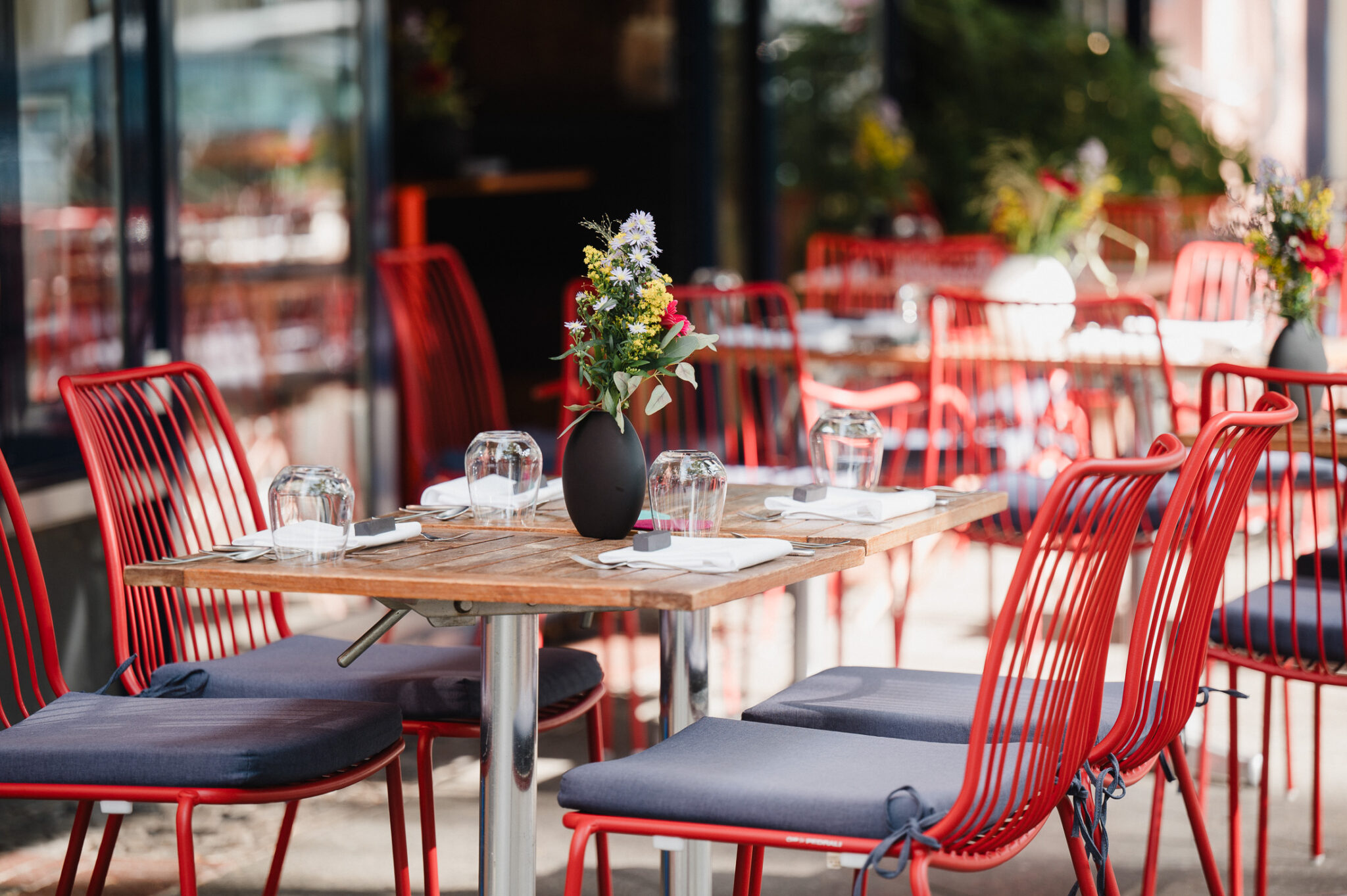 Red outdoor terrace of Restaurant Brikz with wooden tables, red chairs, and floral centerpieces.