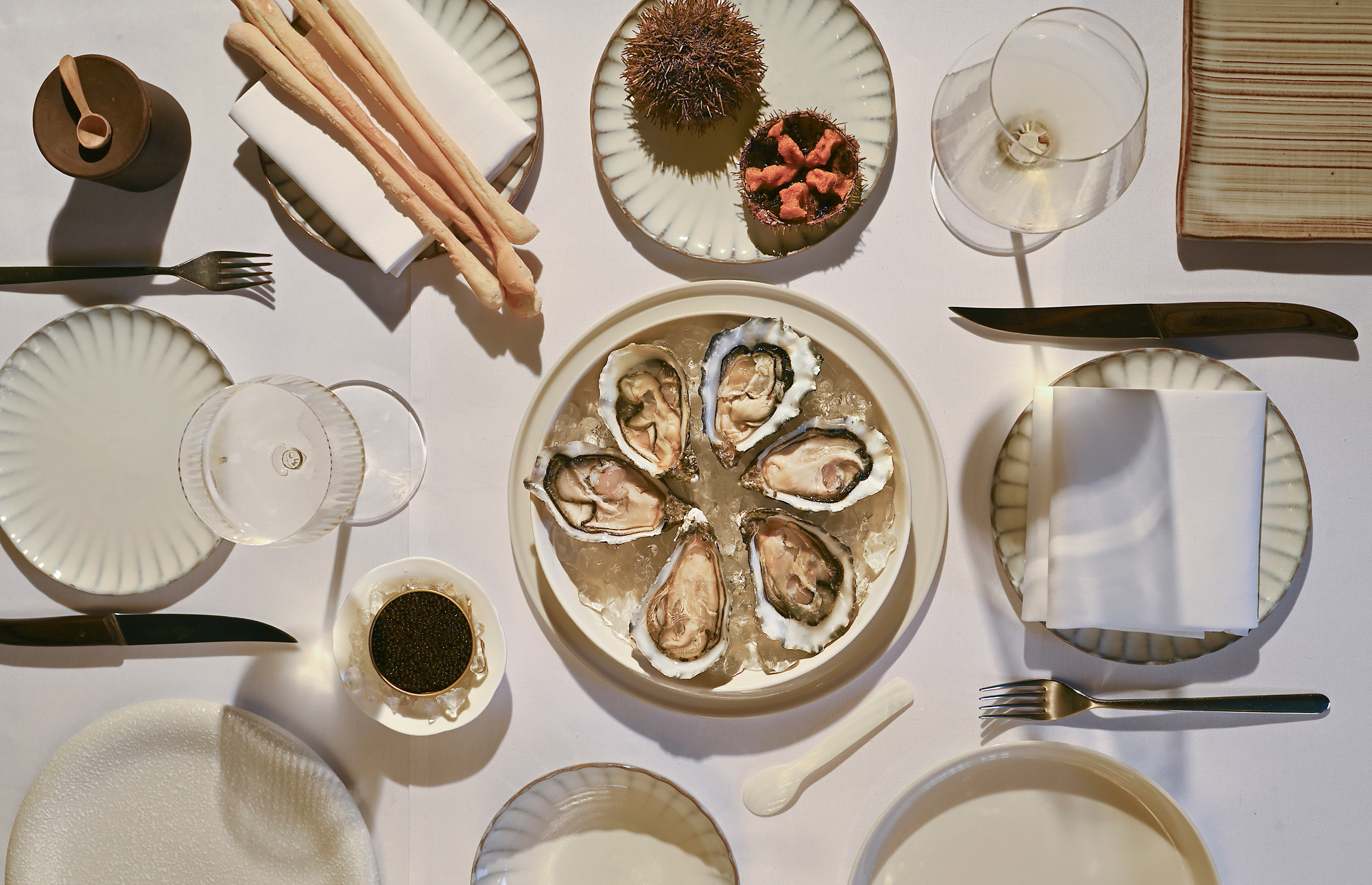 A beautifully arranged dining table featuring oysters on ice, garnished with sea urchin, caviar, and elegant glassware.