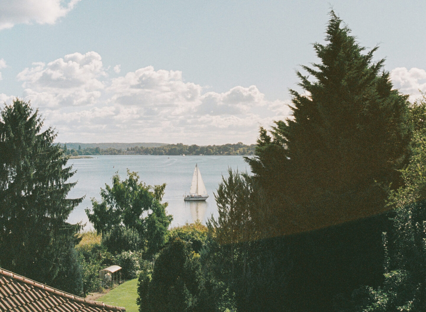 Sailboat on a calm lake surrounded by trees and clouds, viewed from a hilltop in Werder.