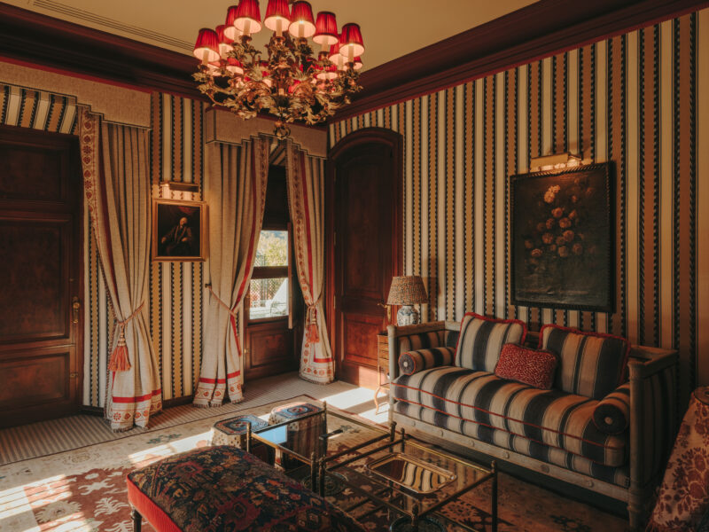 Elegant room with striped wallpaper, a chandelier, a striped sofa, and decorative curtains, featuring a vintage painting.