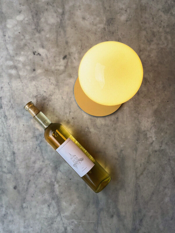 A bottle of white wine next to a round yellow lamp on a marble surface.