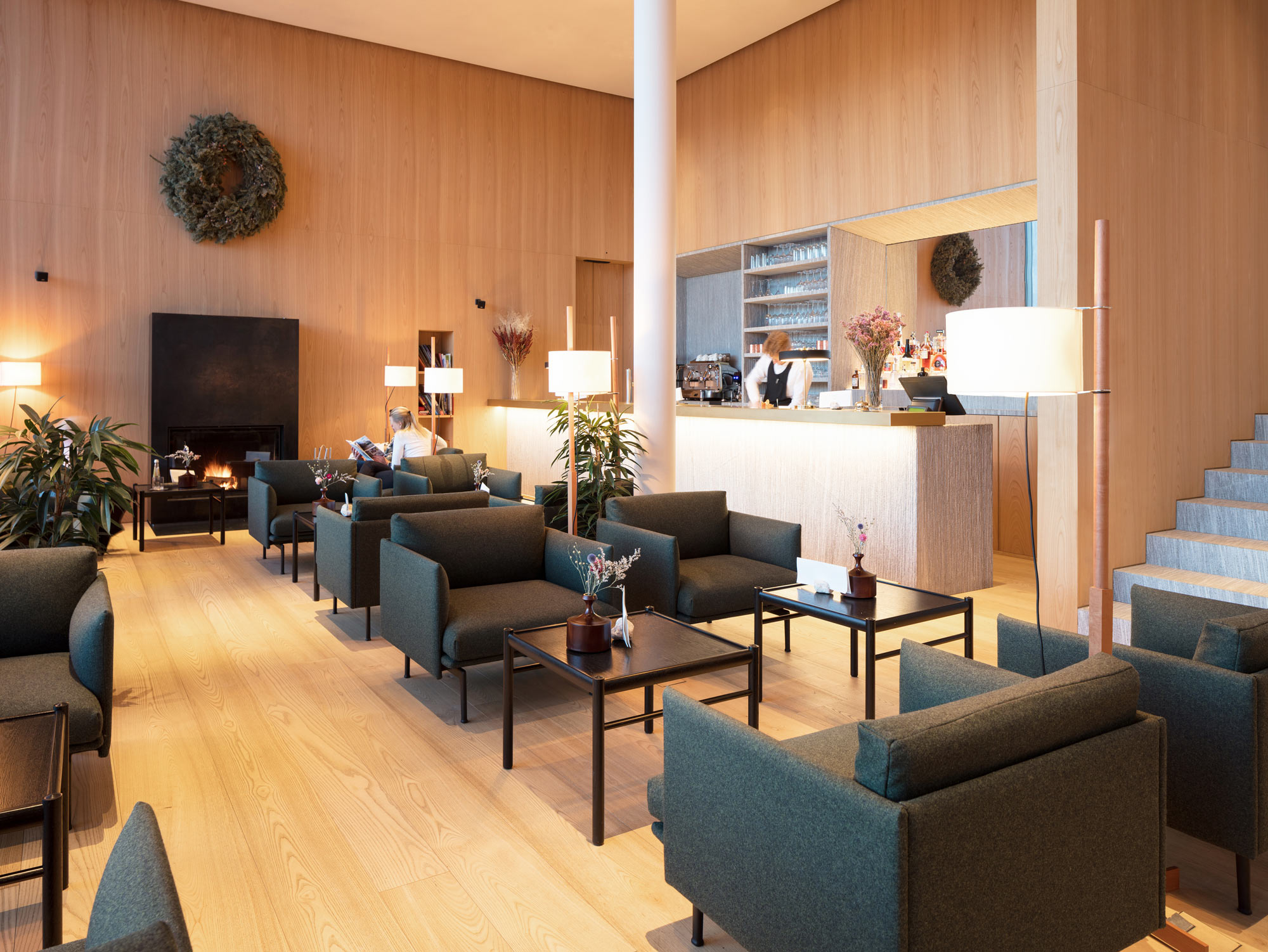 Modern hotel lobby featuring wooden walls, green sofas, and a reception desk with staff, plants, and warm lighting.