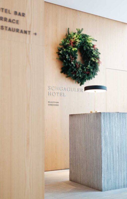 Reception area of Schgaguler Hotel featuring a wooden wall, a decorative wreath, and a modern light fixture.