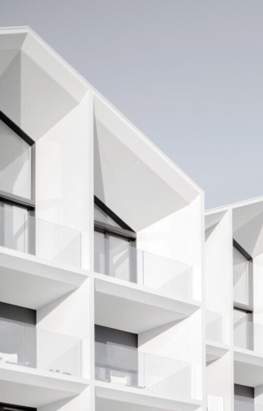 Modern white hotel facade with geometric architecture and large glass balconies.
