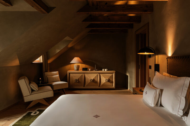 Cozy hotel room at Castel Badia featuring a bed, wooden beams, a lamp, and a seating area.