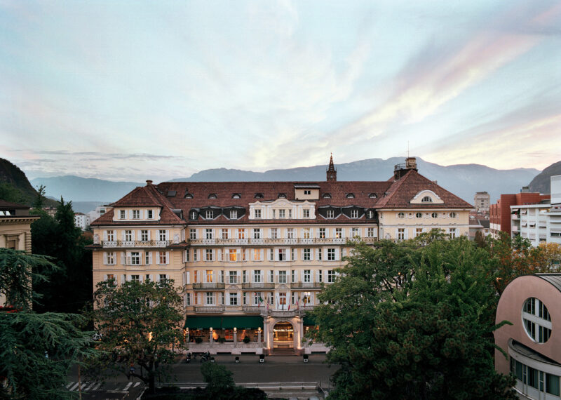 Historic Parkhotel Laurin with a scenic backdrop of mountains and a pastel sky at dusk.