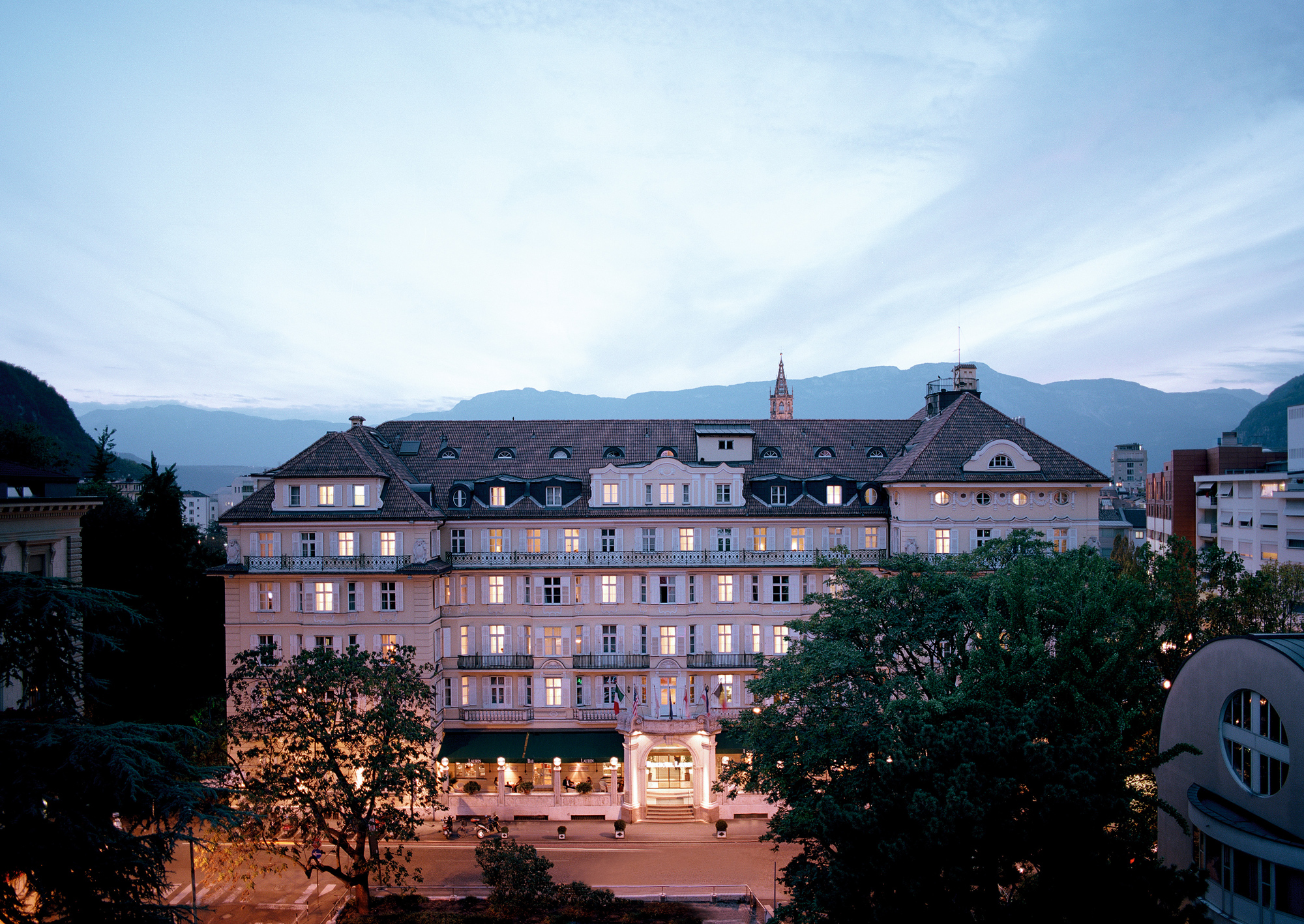 Parkhotel Laurin at dusk, showcasing its elegant facade and surrounding trees against a twilight sky.