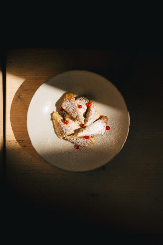 Sliced dessert pieces dusted with powdered sugar and garnished with red sauce on a round plate.