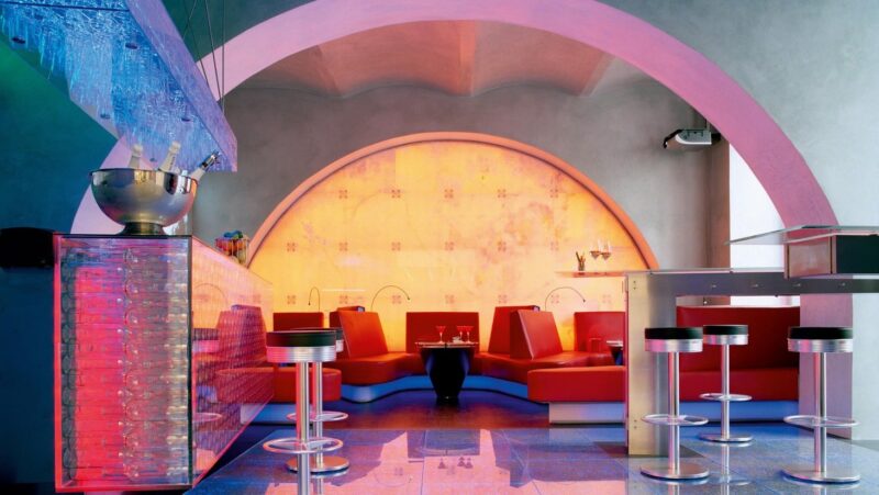 Vibrant lounge area with red seating, colorful lighting, and a stylish bar at Parkhotel Laurin.