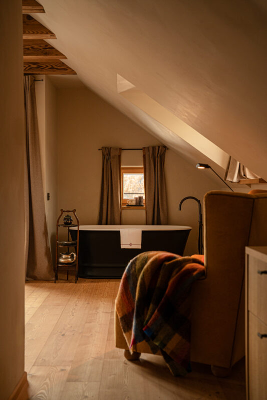 Cozy interior of Castel Badia featuring a black bathtub, wooden floor, and a colorful blanket draped over a chair.