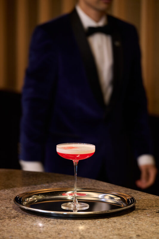 Cocktail on a silver tray with a blurred figure in a tuxedo in the background at The Florentin bar.