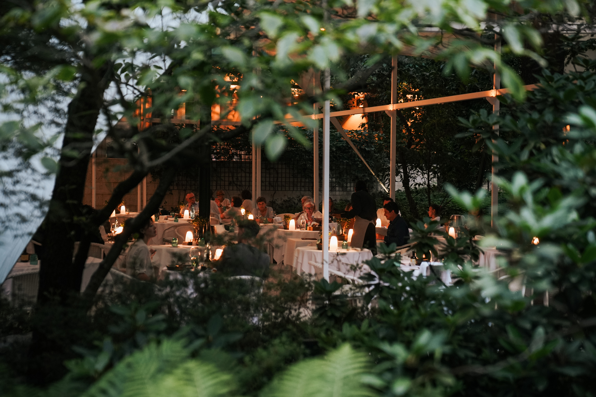 Intimate outdoor dining scene at Parkrestaurant Laurin, surrounded by greenery and softly lit tables.