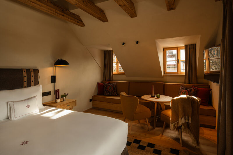 Cozy hotel room at Castel Badia featuring a bed, seating area, and warm lighting with wooden accents.
