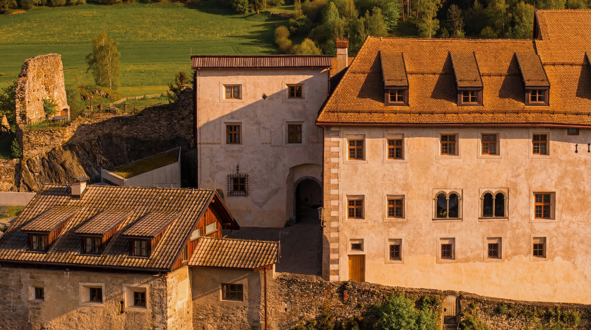 Historic Castel Badia with a mix of stone and plaster architecture, surrounded by lush green fields.