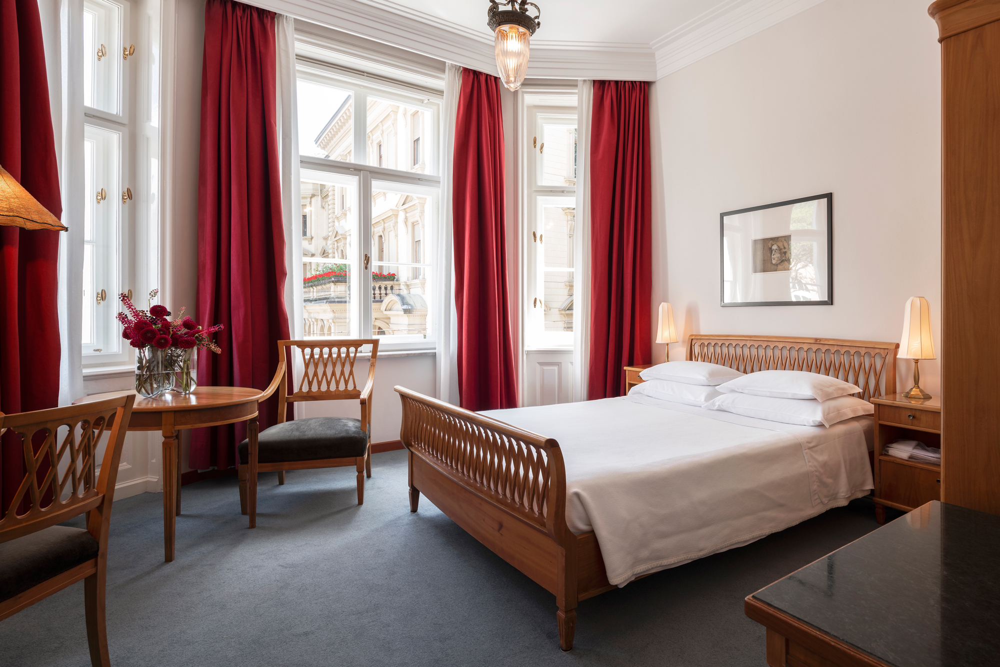 Standard double room at Parkhotel Laurin, featuring a bed, seating area, and large windows with red curtains.