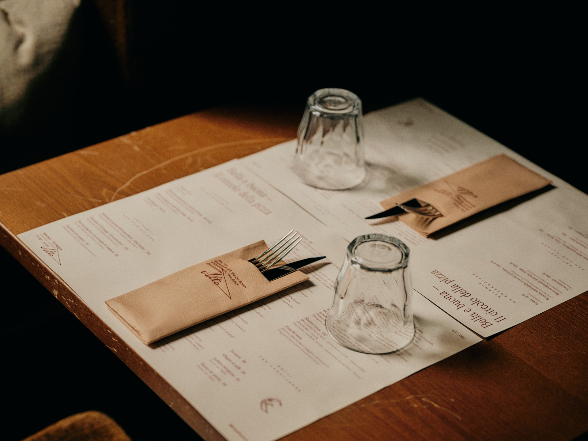 Table setting at Parkhotel Mondschein with two menus, cutlery in pouches, and two glasses on a wooden surface.