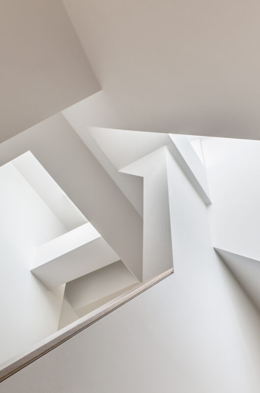 Geometric white interior with angular shapes and skylights, showcasing modern architectural design.