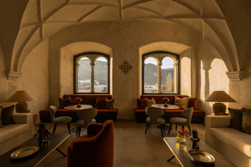 Cozy lounge area in Castel Badia with arched ceilings, elegant furniture, and large windows showcasing a mountain view.