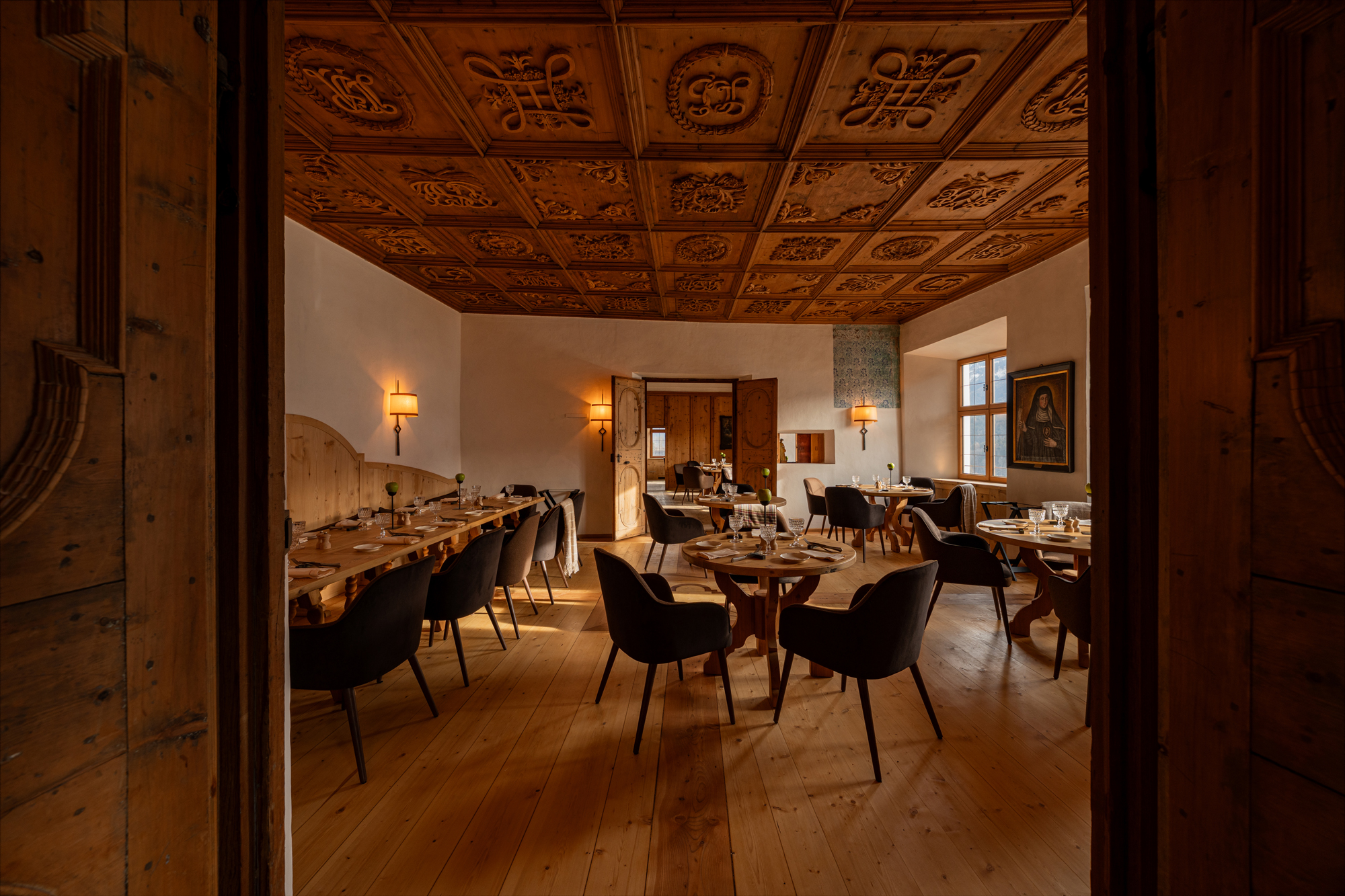 Elegant dining room at Castel Badia featuring wooden ceiling, tables set for guests, and warm lighting.