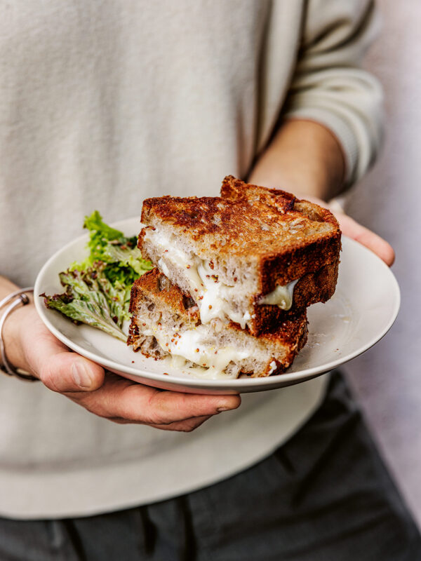 Grilled cheese sandwich with melted cheese, served on a plate with a side of leafy greens.